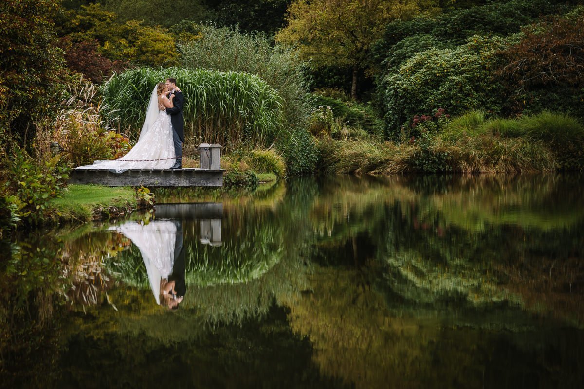 geposeerde trouwfoto bruid bruidegom buiten vijver reflectie water oppervlak groen bomen struiken bruidsfoto portret