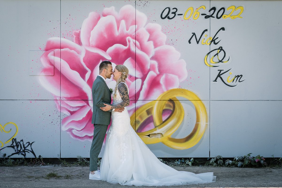 Natuurlijke ongedwongen trouwfoto bruidspaar speciale mural roze rozen trouwringen kleur graffiti_loods_hof Roosendaal documentaire authentieke journalistieke bruidsfotografie trouwfotograaf brabant