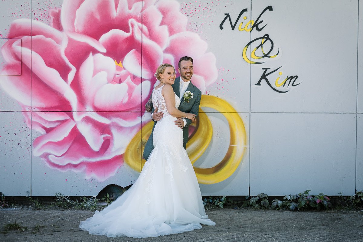 Natuurlijke ongedwongen trouwfoto bruidspaar speciale mural roze rozen trouwringen kleur graffiti_loods_hof Roosendaal documentaire authentieke journalistieke bruidsfotografie trouwfotograaf brabant