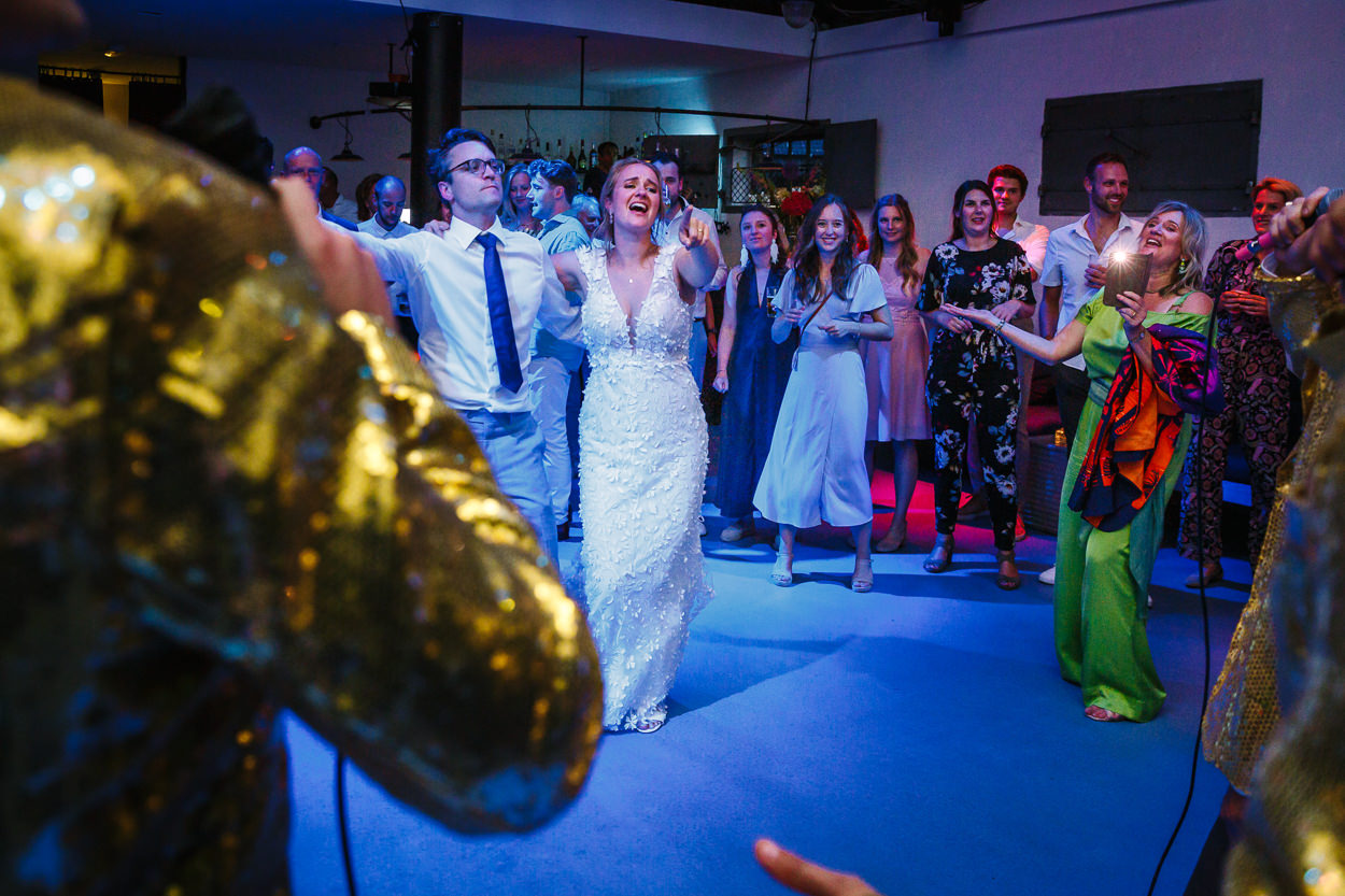 bruid en bruidegom zingen mee met optredende zangers tijdens trouwfeest ongedwongen bruidsfotografie natuurlijke spontane trouwfoto documentair trouwfotograaf bruidsfotograaf breda rijk_van_de_keizer amsterdam